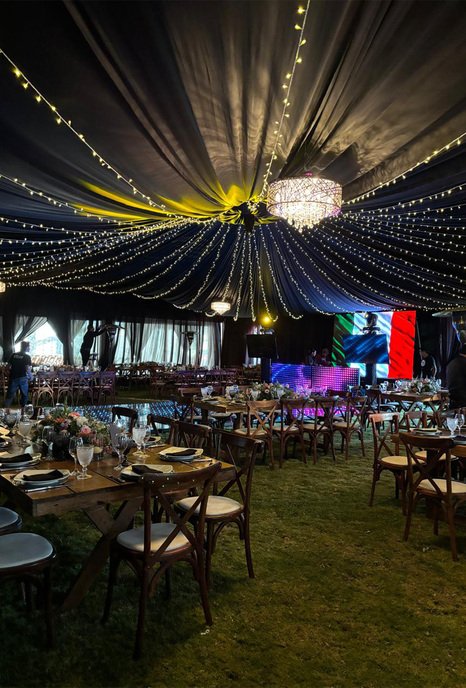 Carpa de recepción con iluminación morada y mesas redondas para banquete de boda