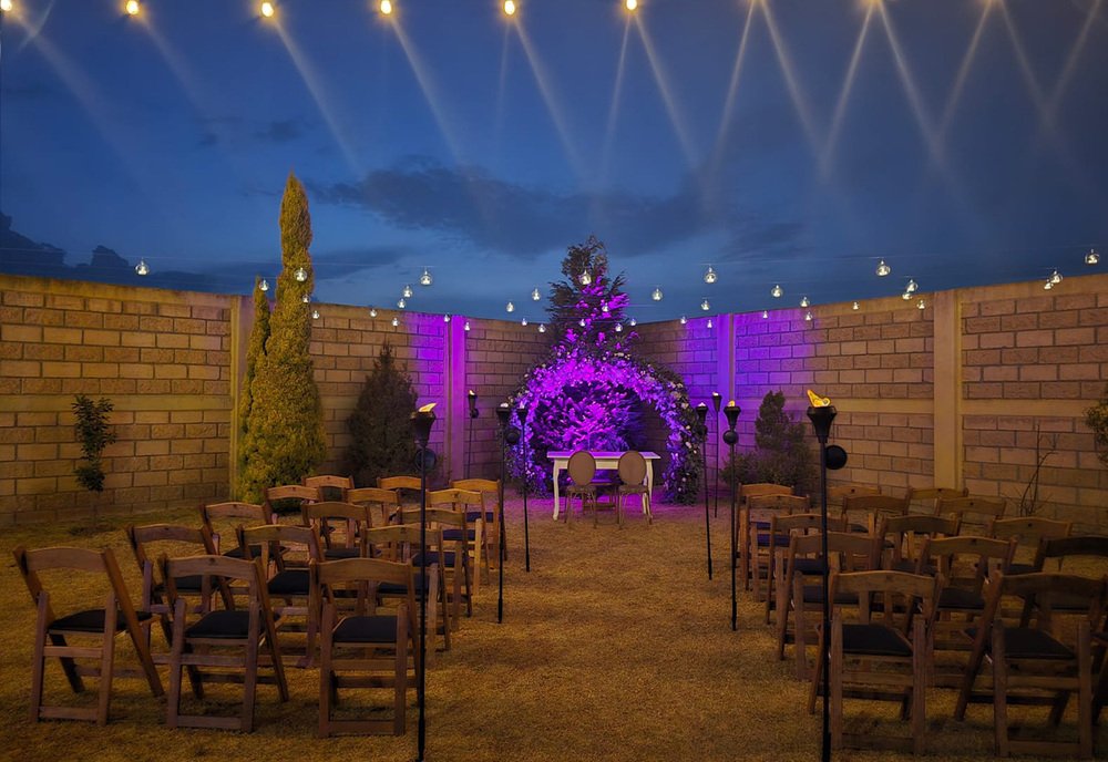 Ceremonia nocturna al aire libre con arco floral iluminado en tonos morados en Sakura Metepec