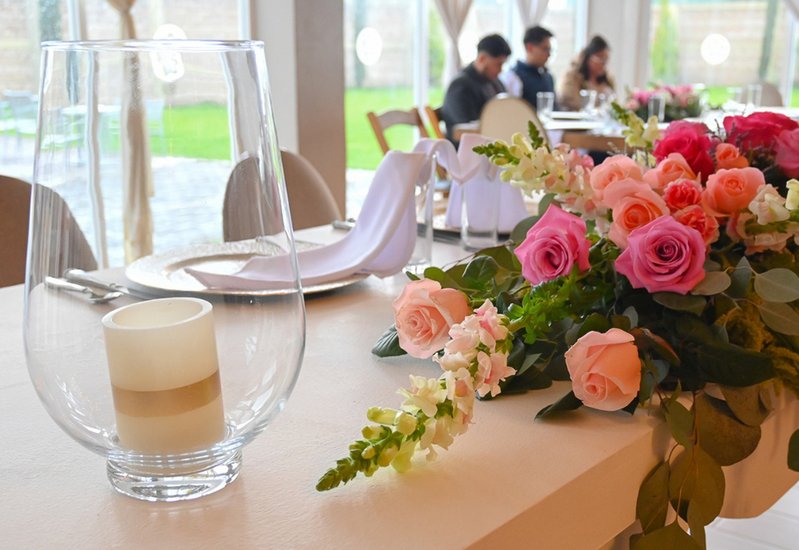 Centro de mesa con rosas rosas y copa de vino en recepción de boda