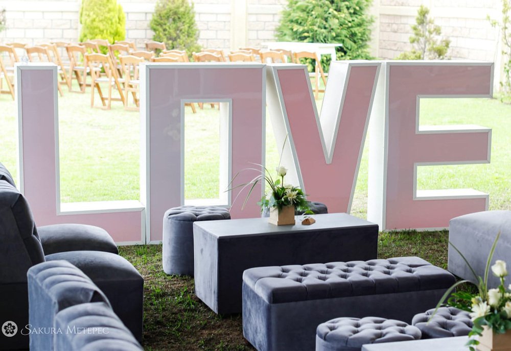 Lounge exterior con letras decorativas de LOVE y luces de bistró para recepción de boda
