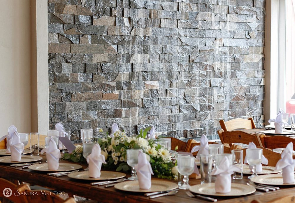 Mesa decorada con centro floral blanco frente a muro de piedra en boda en Sakura Metepec