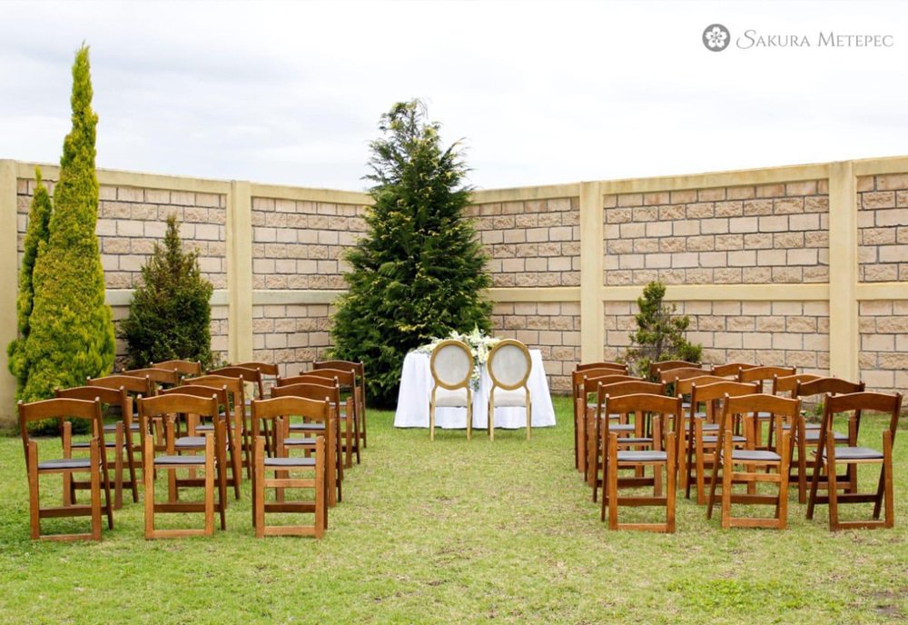 Ceremonia al aire libre con sillas nupciales decoradas con flores en el jardín de Sakura Metepec