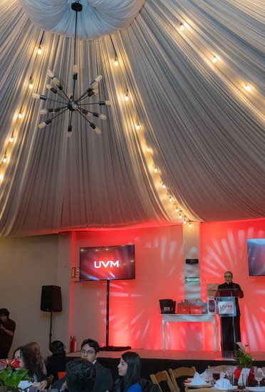 Salón entelado con iluminación roja y pantalla UVM durante evento institucional en Metepec