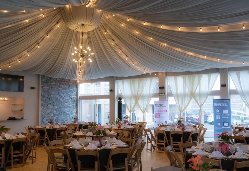 Salón entelado con mesas redondas, candelabro y luces cálidas listo para evento empresarial