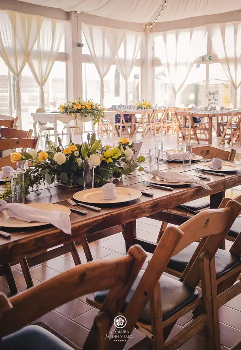 Mesa de madera con centro floral amarillo en el salón de cristal de Sakura Metepec