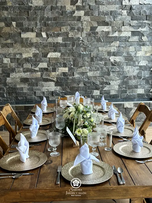 Mesa de madera con platos base dorados frente al muro de piedra del salón Sakura
